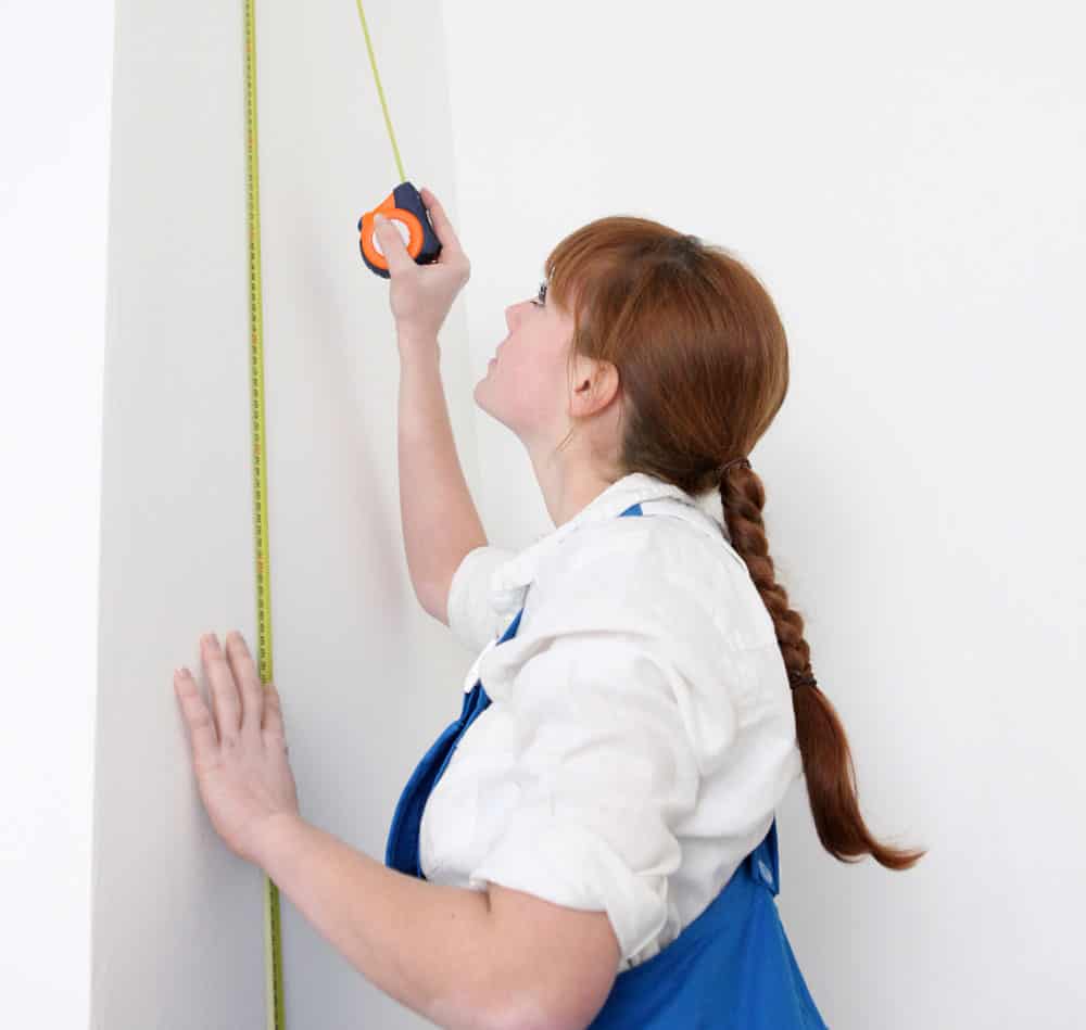 Lady measuring and marking wall space for installing peel and stick wallpaper prints